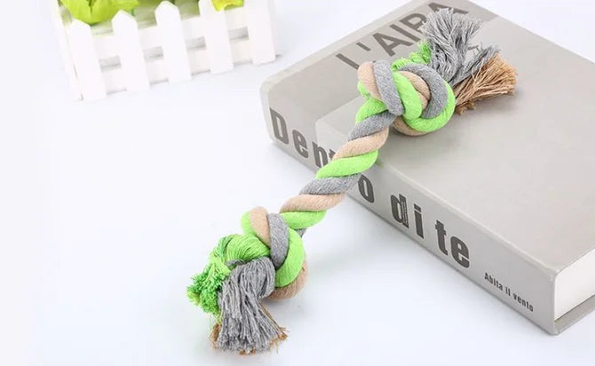 Green and gray braided pet toy on a white surface with a book in the background.