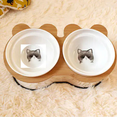 Double pet bowl with wooden base featuring a cartoon cat design on a soft surface.