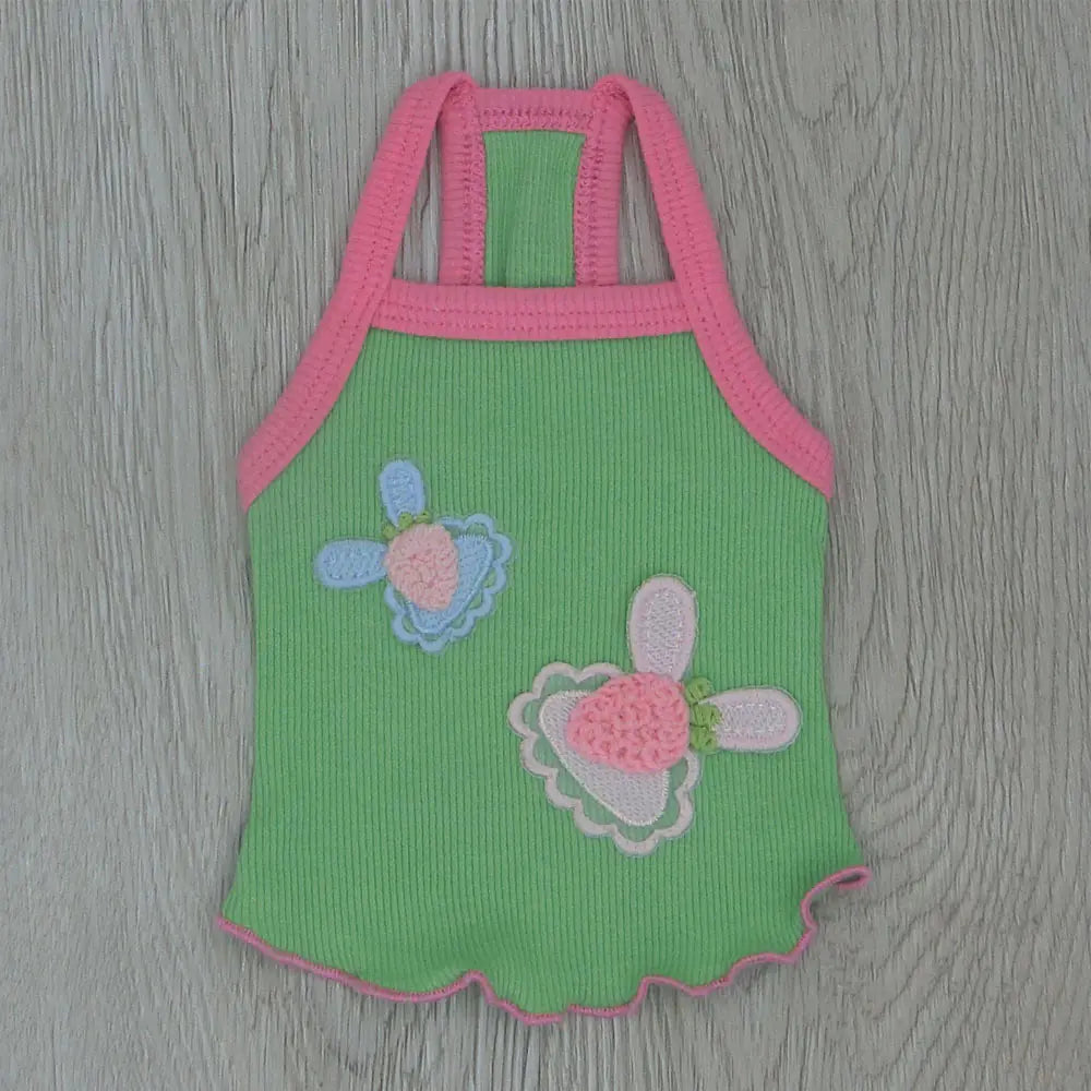 Green baby romper with pink straps and floral designs on a wooden surface