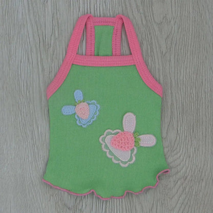 Green baby romper with pink straps and floral designs on a wooden surface