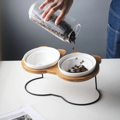 Person pouring food into a modern pet feeder with two bowls on a white surface.