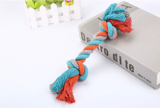 Colorful braided rope toy on a white surface with a book in the background