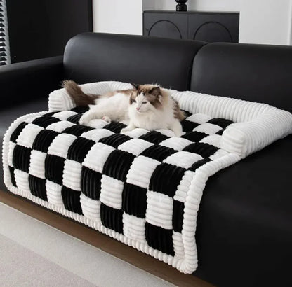 Two cats on a black and white checkered pet bed on a black sofa.
