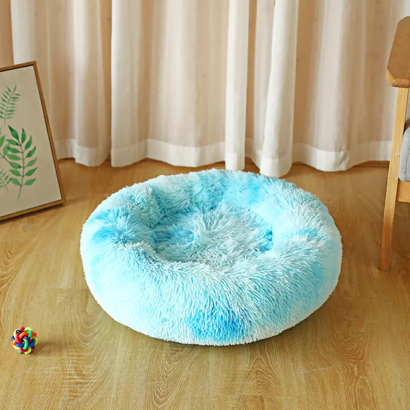 Fluffy blue pet bed on a wooden floor with curtains in the background