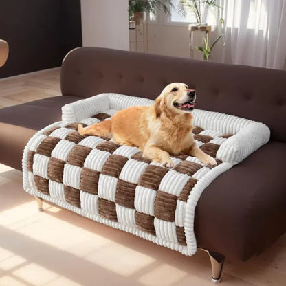 Dog lying on a checkered pet bed on a brown sofa in a bright room.